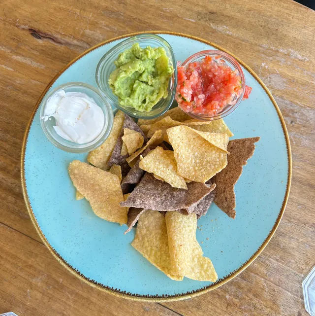 Totopos con guacamole, salsa roja y crema en un plato turquesa